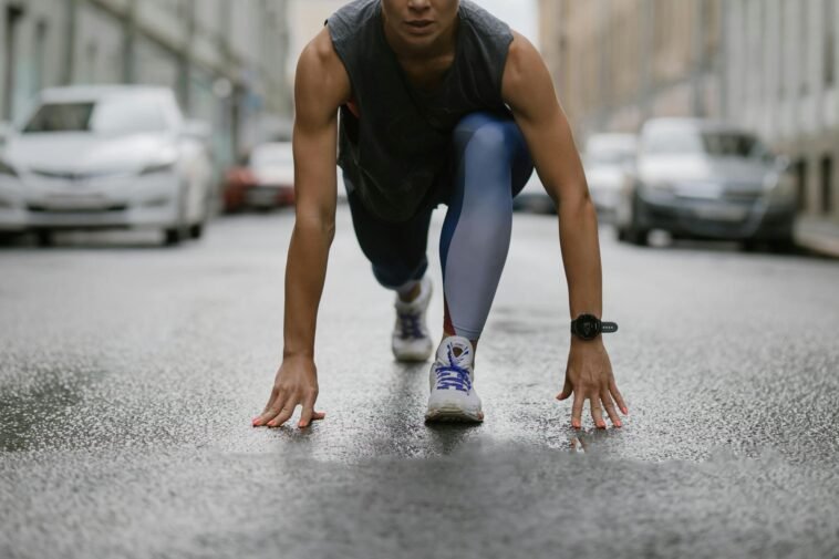 Determined woman in athletic pose ready to sprint on a wet city street.