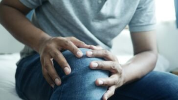 Close-up of a man holding his knee, capturing a moment of discomfort in a casual indoor setting.