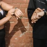 Two people in sportswear checking their fitness trackers outdoors against a brick wall.