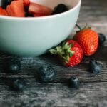 Close-up of fresh strawberries and blueberries in a ceramic bowl on a rustic wooden table.