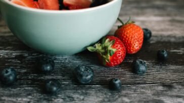 Close-up of fresh strawberries and blueberries in a ceramic bowl on a rustic wooden table.