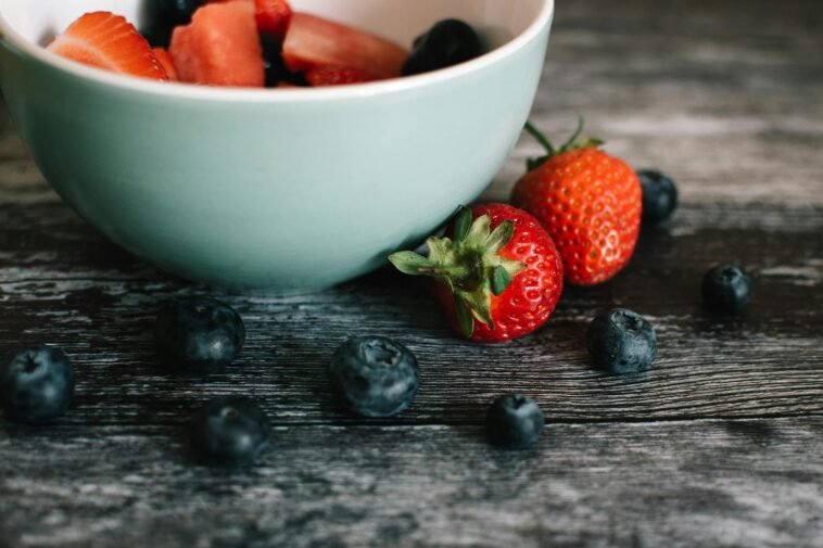 Close-up of fresh strawberries and blueberries in a ceramic bowl on a rustic wooden table.