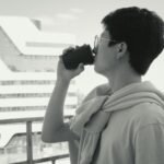 Side view of a man sipping coffee on a balcony, overlooking a modern cityscape.