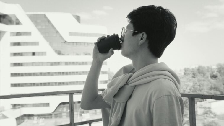 Side view of a man sipping coffee on a balcony, overlooking a modern cityscape.