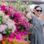 Joyful senior woman wearing sunglasses next to a colorful flower bush outdoors.