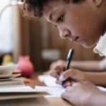 A young boy intensely writing indoors, capturing a moment of concentration.