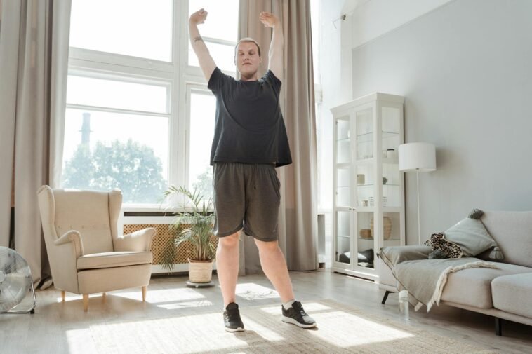 A young man enjoying a morning stretch in a bright, airy living room, embracing a healthy lifestyle.