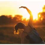 A woman performs a stretching exercise outdoors at sunrise, embracing fitness during the serene golden hour.