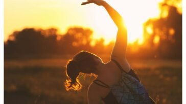 A woman performs a stretching exercise outdoors at sunrise, embracing fitness during the serene golden hour.