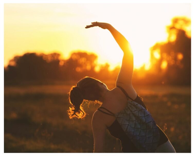 A woman performs a stretching exercise outdoors at sunrise, embracing fitness during the serene golden hour.