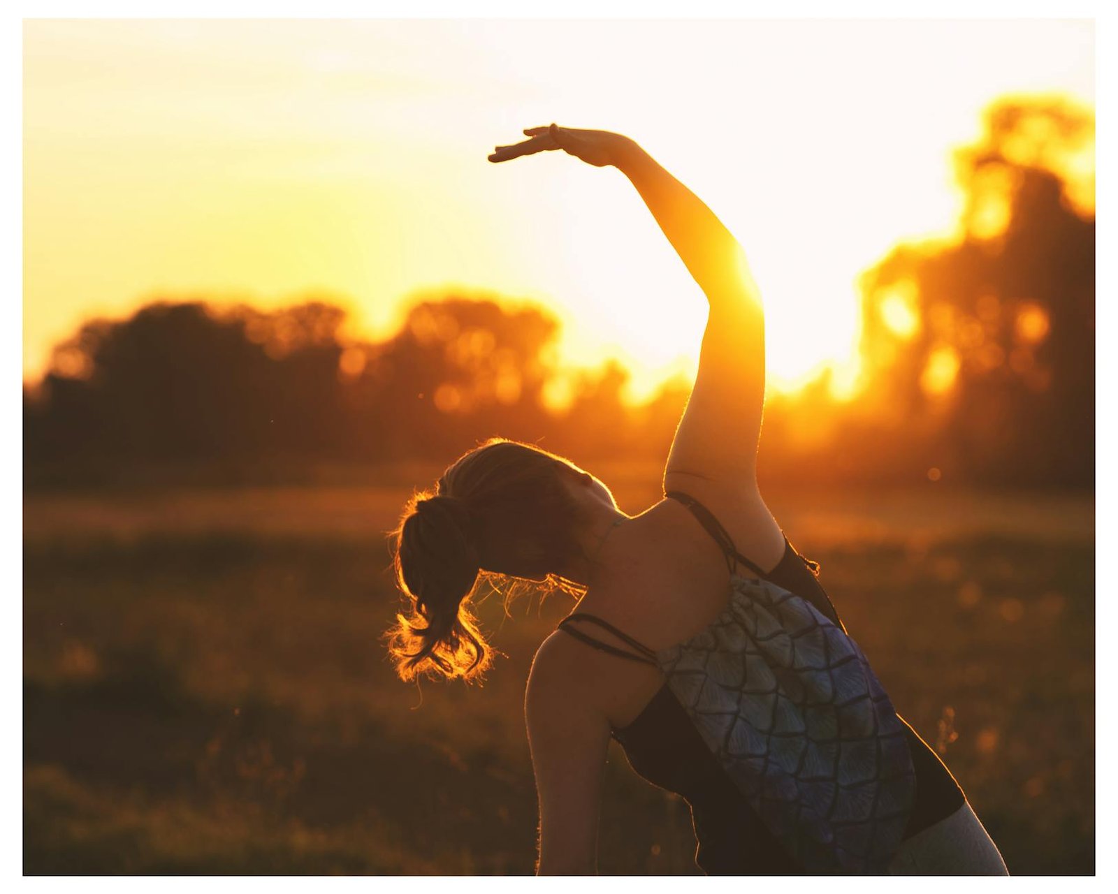 A woman performs a stretching exercise outdoors at sunrise, embracing fitness during the serene golden hour.