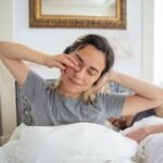 Young woman waking up with a morning stretch, captured indoors with natural light.