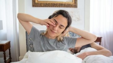 Young woman waking up with a morning stretch, captured indoors with natural light.
