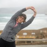 Senior woman stretching outdoors by the seaside in Portugal, embracing a healthy lifestyle.