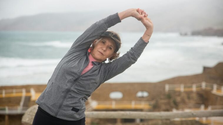Senior woman stretching outdoors by the seaside in Portugal, embracing a healthy lifestyle.