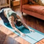 A woman performs a yoga pose on a mat in a sunny living room, focusing on relaxation.