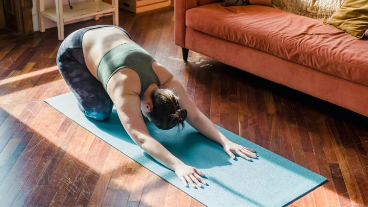 A woman performs a yoga pose on a mat in a sunny living room, focusing on relaxation.