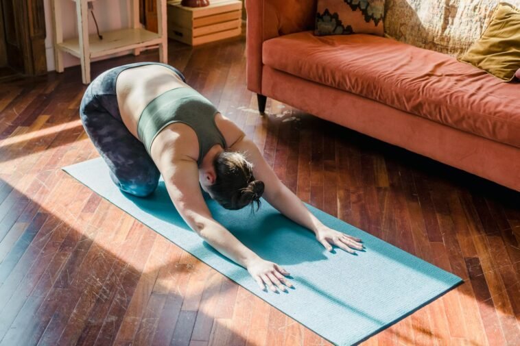 A woman performs a yoga pose on a mat in a sunny living room, focusing on relaxation.