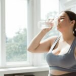 Active woman in sportswear drinks water indoors. Healthy lifestyle and hydration.