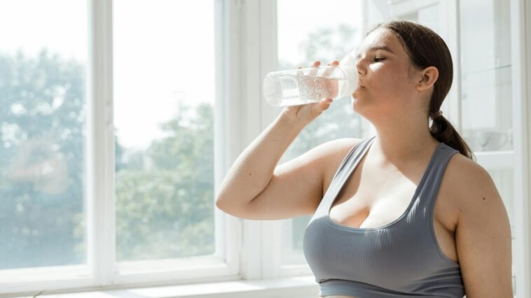Active woman in sportswear drinks water indoors. Healthy lifestyle and hydration.
