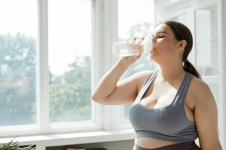 Active woman in sportswear drinks water indoors. Healthy lifestyle and hydration.