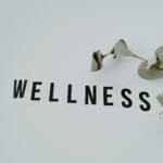 Minimalist image of the word 'wellness' with eucalyptus branch, creating a serene vibe on white background.