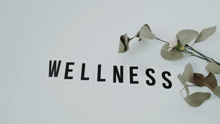 Minimalist image of the word 'wellness' with eucalyptus branch, creating a serene vibe on white background.