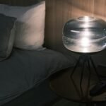 Illuminated bedside table with modern glass lamp and pillows at night.