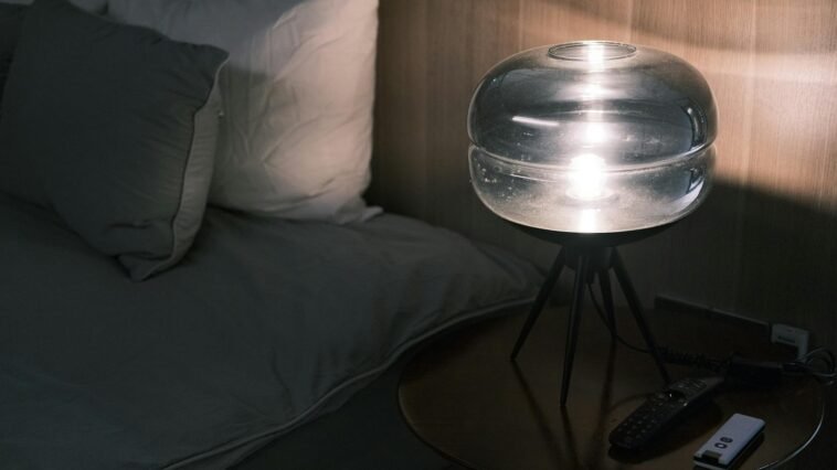 Illuminated bedside table with modern glass lamp and pillows at night.