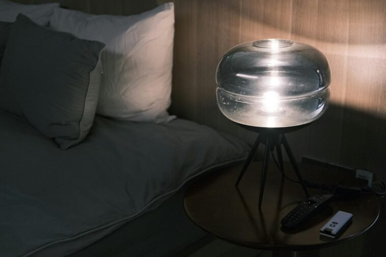 Illuminated bedside table with modern glass lamp and pillows at night.