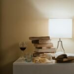 A minimalist bedroom nightstand with books, a lamp, and a glass of wine for a cozy evening vibe.