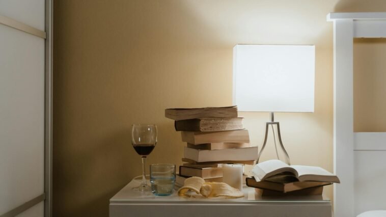 A minimalist bedroom nightstand with books, a lamp, and a glass of wine for a cozy evening vibe.