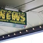 From below of illuminated signboard with news papers magazines inscriptions hanging on metal ceiling on street