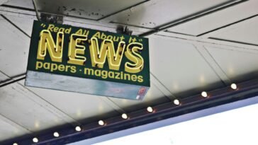 From below of illuminated signboard with news papers magazines inscriptions hanging on metal ceiling on street