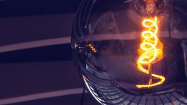 Artistic close-up of an illuminated light bulb with glowing filament and reflections.