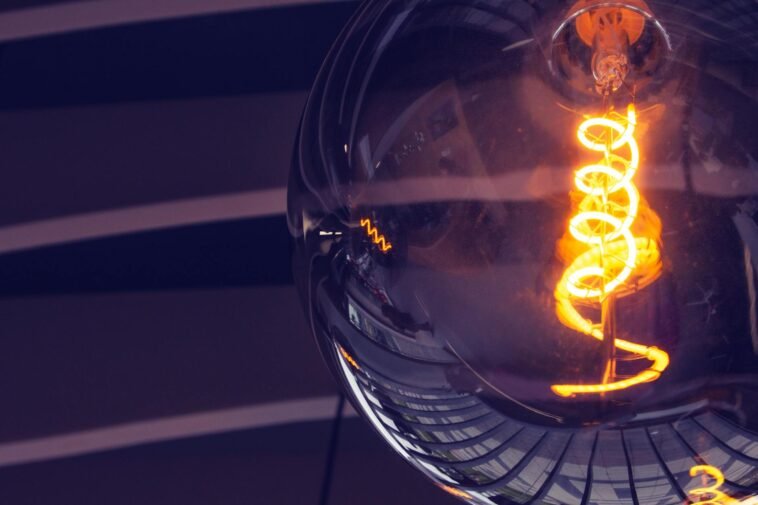 Artistic close-up of an illuminated light bulb with glowing filament and reflections.