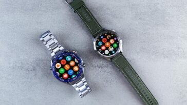 Two smart watches with colorful interfaces displayed on a sleek gray textured surface.
