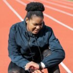 A woman in activewear on a running track checks her smartwatch after a workout.