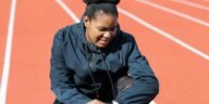 A woman in activewear on a running track checks her smartwatch after a workout.