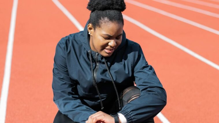 A woman in activewear on a running track checks her smartwatch after a workout.
