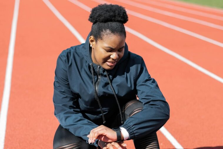 A woman in activewear on a running track checks her smartwatch after a workout.