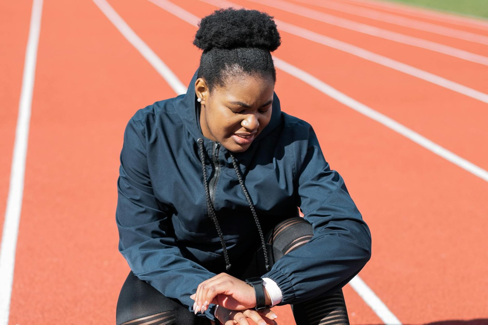 A woman in activewear on a running track checks her smartwatch after a workout.