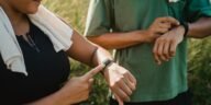 Two people checking their fitness watches while taking a break from a workout outside.