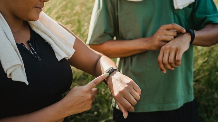 Two people checking their fitness watches while taking a break from a workout outside.