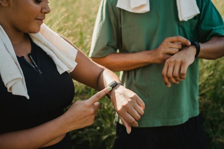 Two people checking their fitness watches while taking a break from a workout outside.