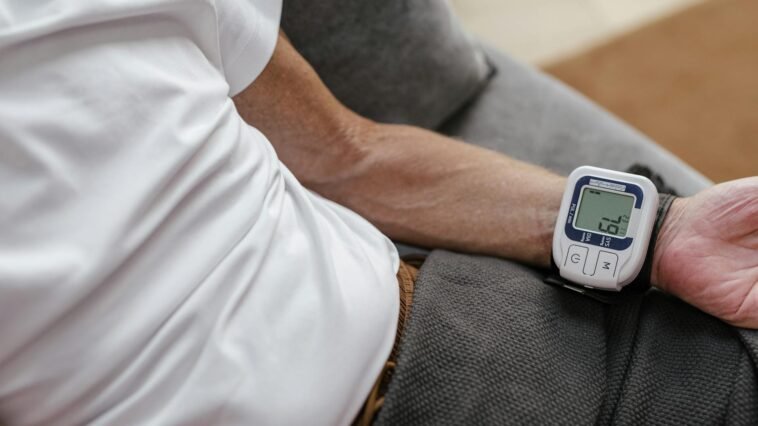 Adult man using a wrist blood pressure monitor to measure blood pressure at home.
