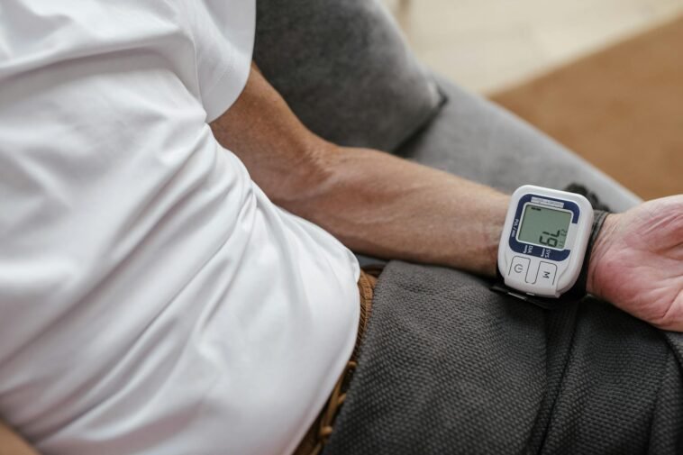 Adult man using a wrist blood pressure monitor to measure blood pressure at home.