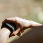 From above of crop anonymous person wearing modern bracelet with small display while standing outdoors on blurred background in daylight
