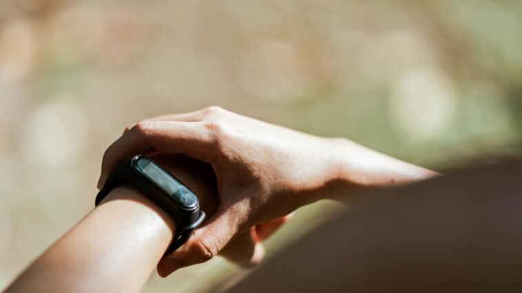 From above of crop anonymous person wearing modern bracelet with small display while standing outdoors on blurred background in daylight