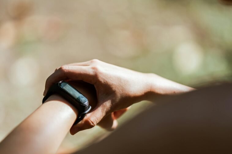 From above of crop anonymous person wearing modern bracelet with small display while standing outdoors on blurred background in daylight